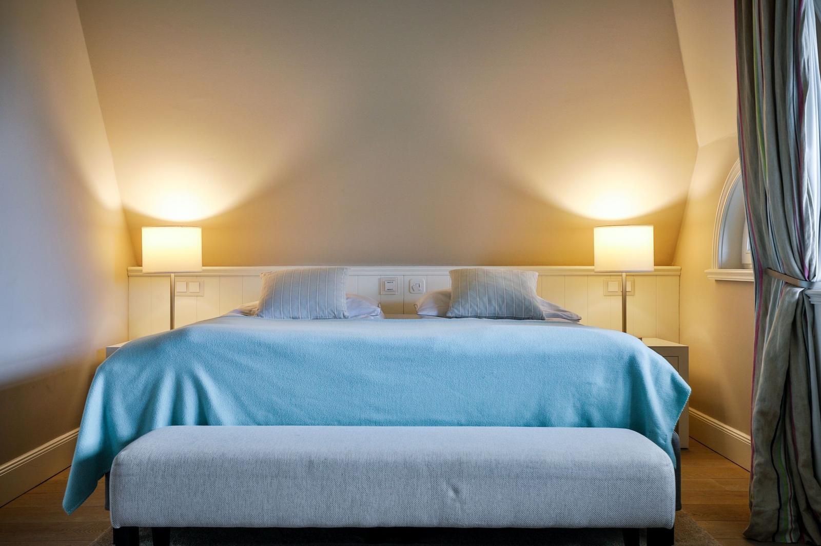 Schlafzimmer mit Bett, blauer Decke und zwei Nachttischen mit Lampen.