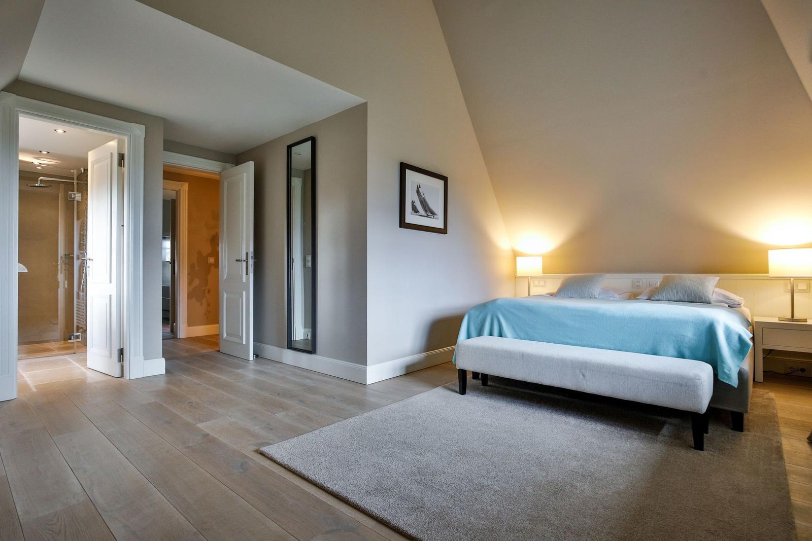 Schlafzimmer mit Bett, Teppich und Blick in Bad und Flur.