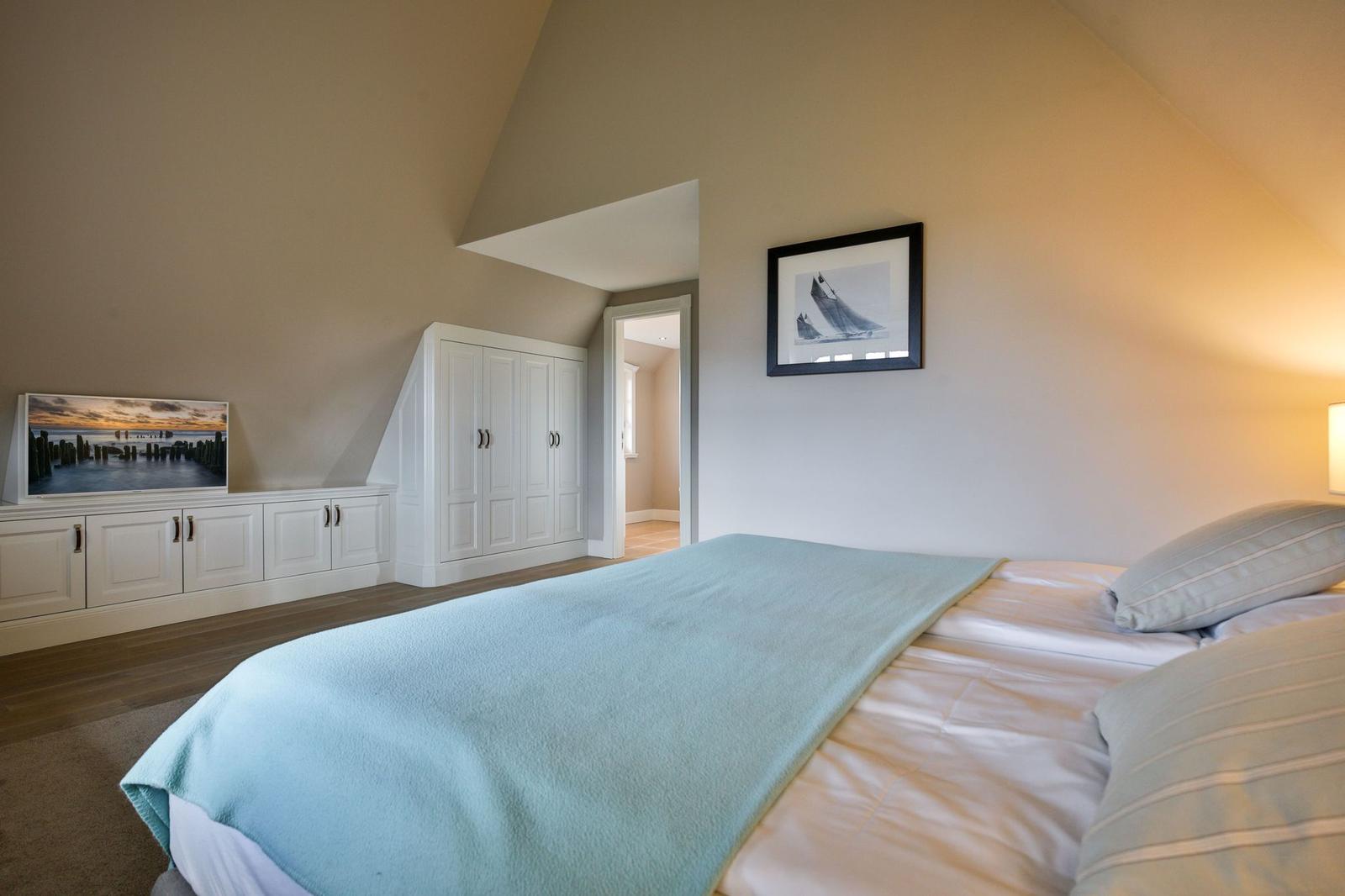 Schlafzimmer mit Bett, Kleiderschrank und Fernseher an der Wand.