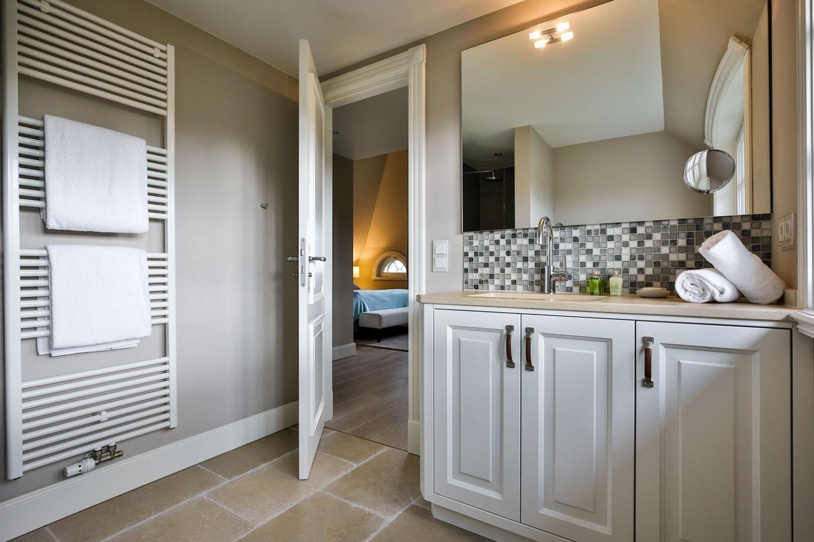 Badezimmer mit Waschbecken, Spiegel und Handtuchheizkörper. Tür führt in Schlafzimmer.