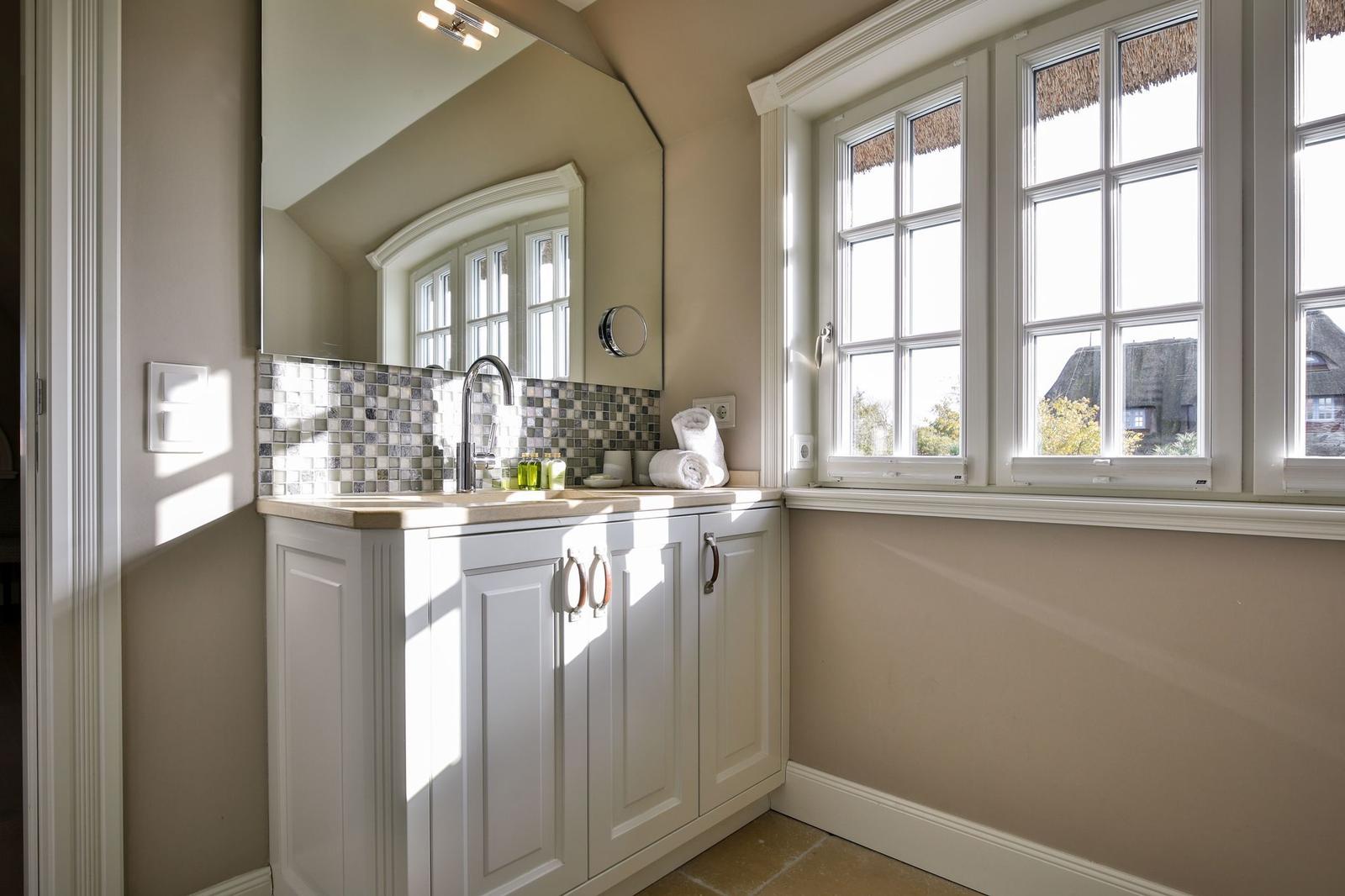 Badezimmer mit Waschbecken, Spiegel und Fenster