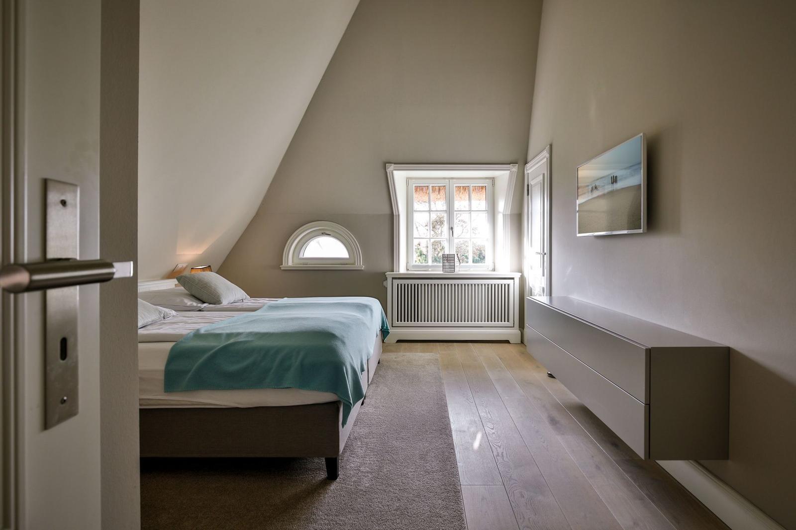 Schlafzimmer mit Dachschräge, Bett, Fenster und Wandbild.