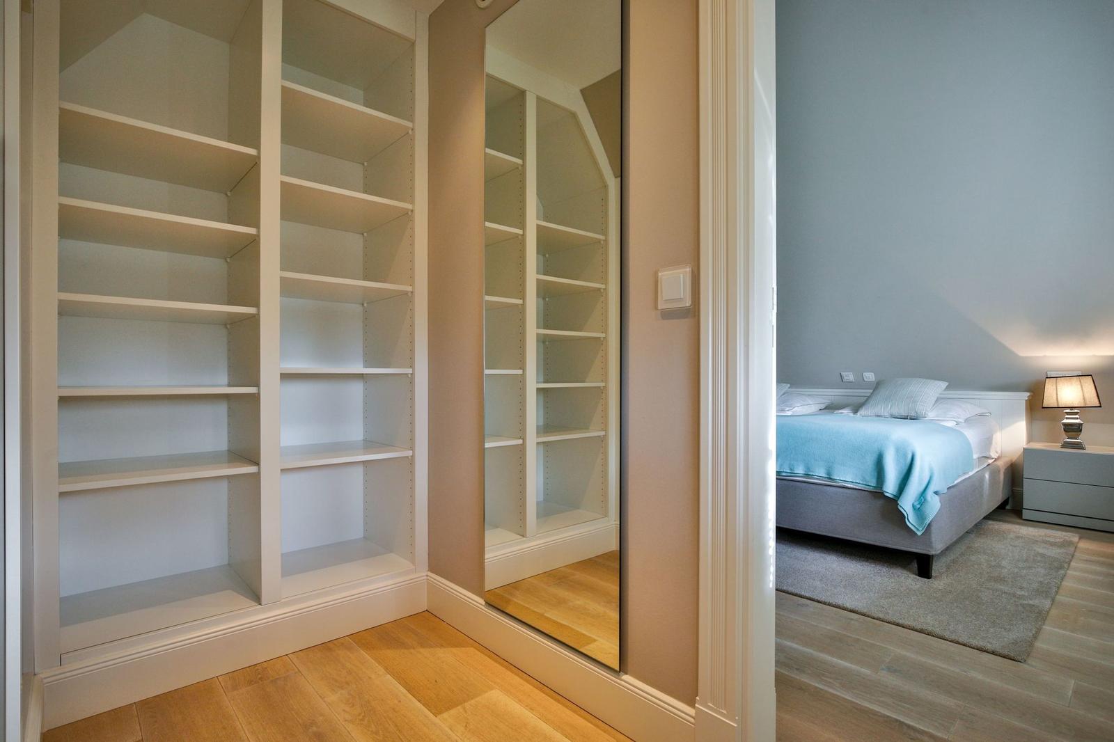 Schlafzimmer mit Bett, Nachttisch und Spiegelschrank. Holzboden und Wandspiegel sichtbar.
