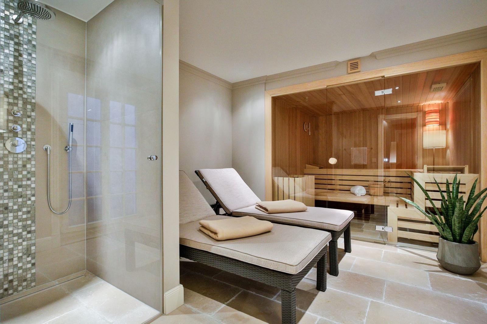 Dusche mit Mosaikwand, zwei Liegestühle und Sauna mit Holzverkleidung.