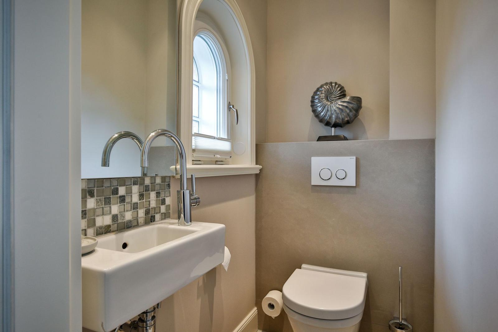 Badezimmer mit Waschbecken, Spiegel und Toilette. Fenster und Mosaikwand.