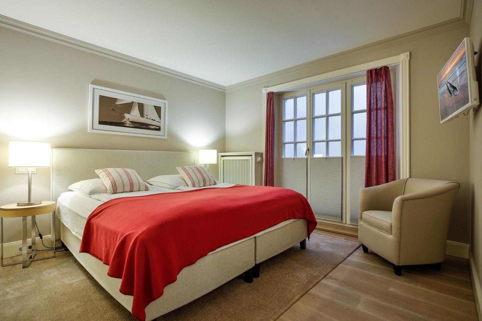 Schlafzimmer mit Doppelbett, Sessel und Fenster zur Terrasse.
