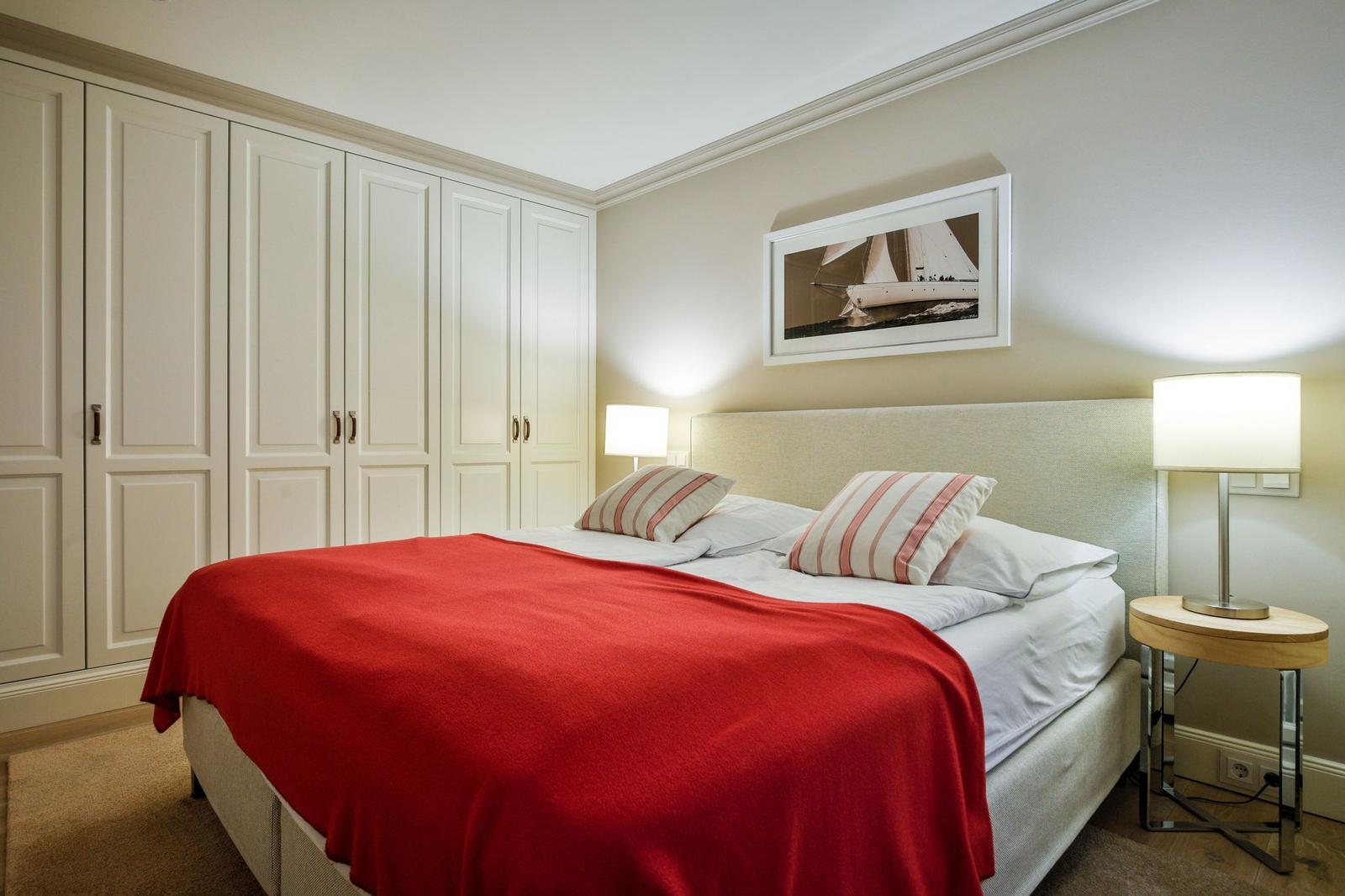 Schlafzimmer mit Bett, rotem Decken, Schrank und Nachttisch mit Lampe.