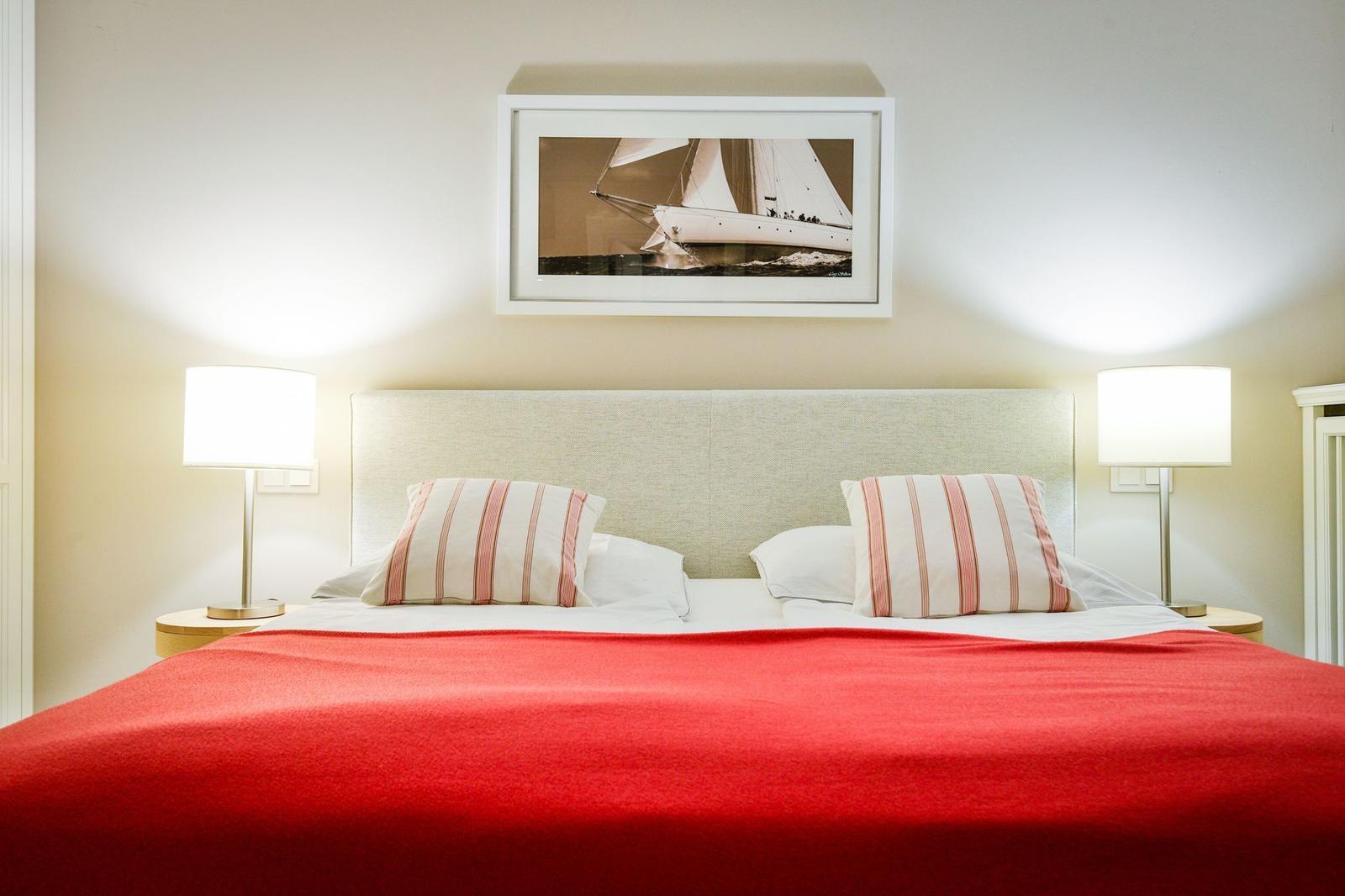 Doppelbett mit roter Decke, zwei Nachttische und Wandbild mit Segelyacht.