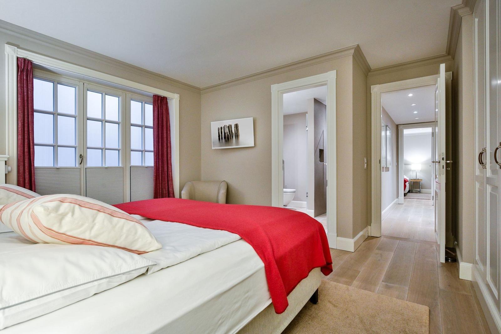 Schlafzimmer mit Bett, Fenster und Blick in Bad und Flur.