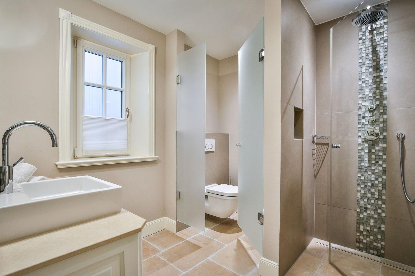 Badezimmer mit Dusche, Toilette und Waschbecken. Fenster mit Jalousie.
