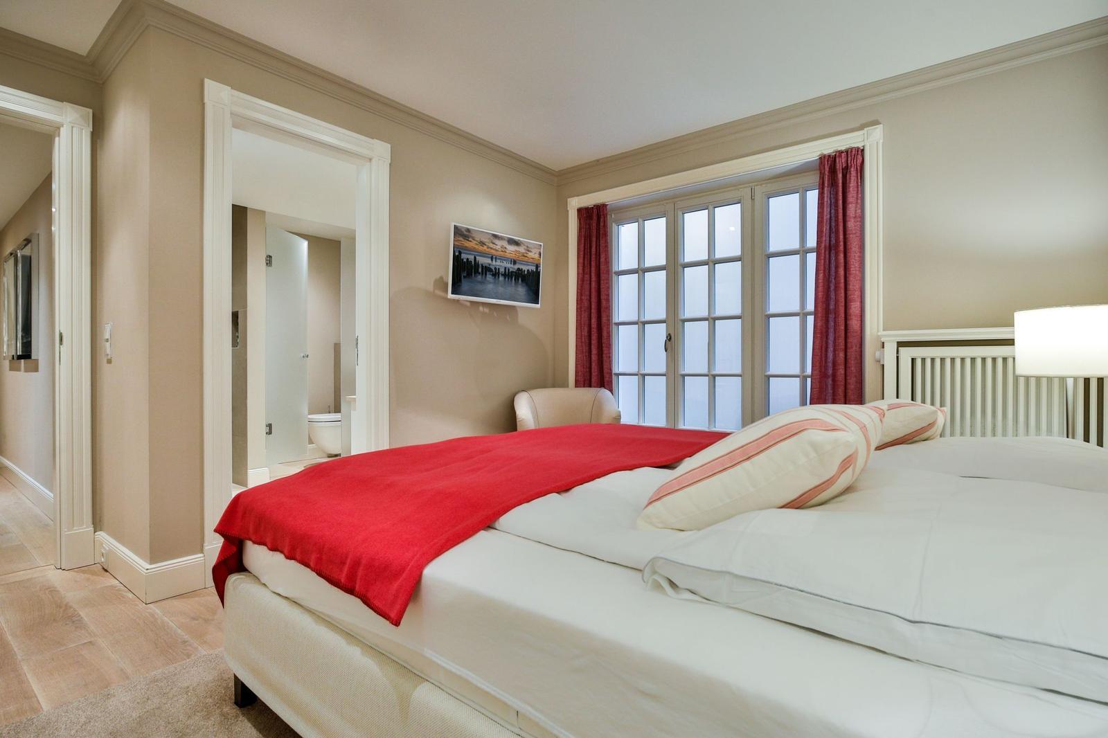 Schlafzimmer mit Bett, Fenster und Bad. Rote Decke und Vorhänge.
