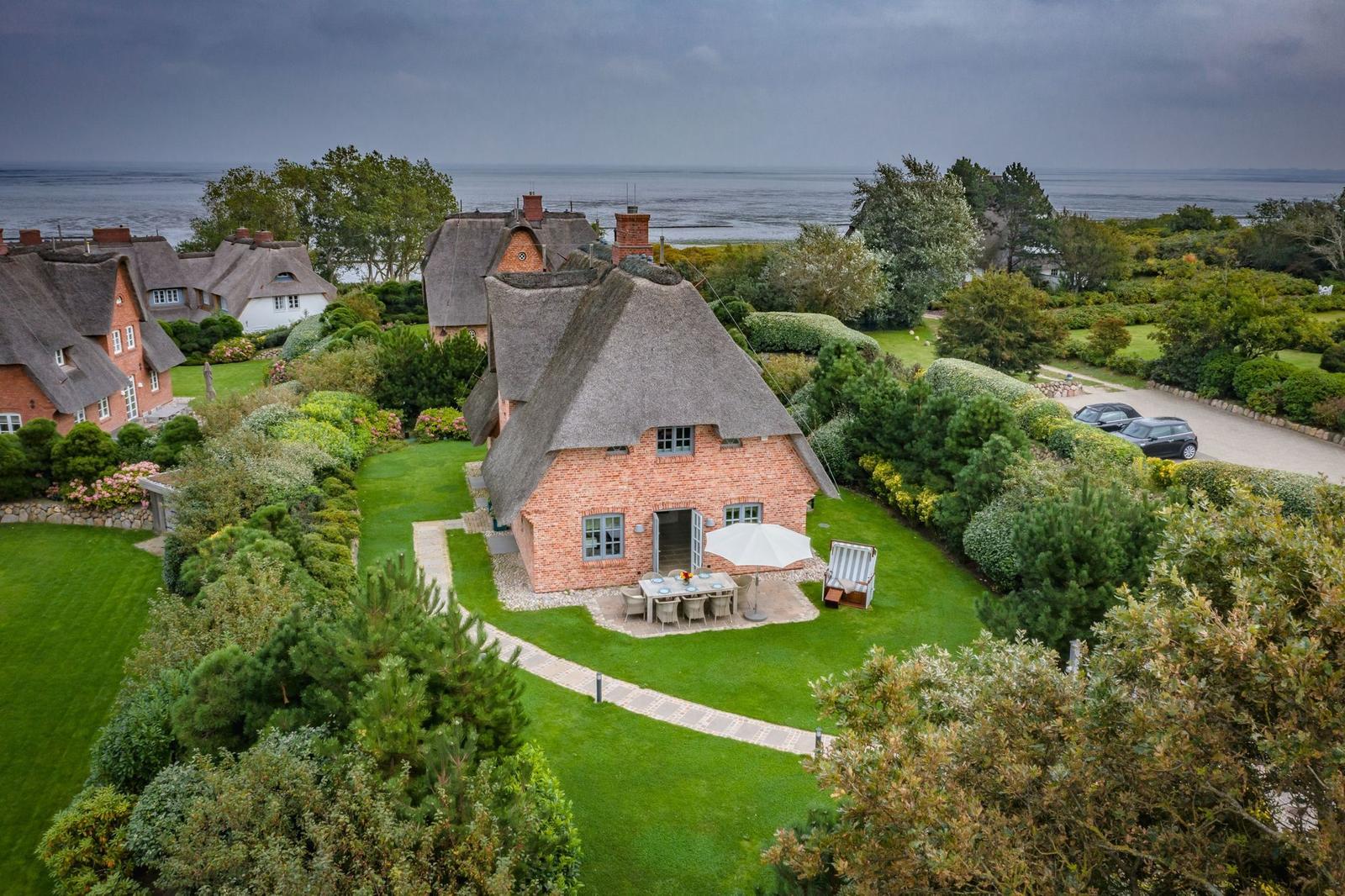 Rotes Backsteinhaus mit Strohdach, Garten und Blick aufs Meer.