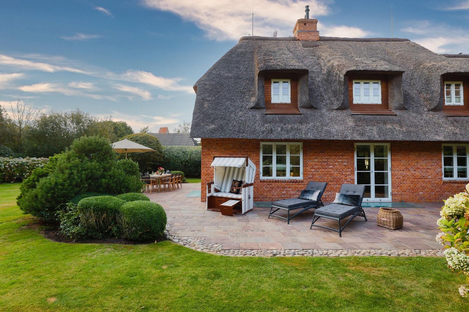 Haus mit Strohdach, Terrasse, Liegen und Garten.