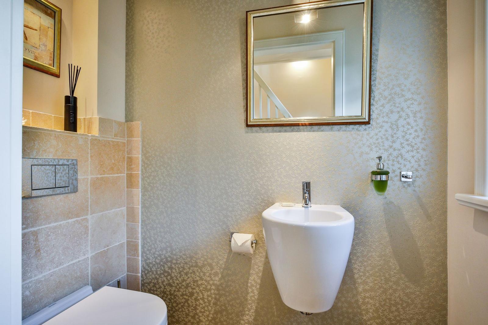 Badezimmer mit Wandspiegel, Hängewaschbecken und Toilette.