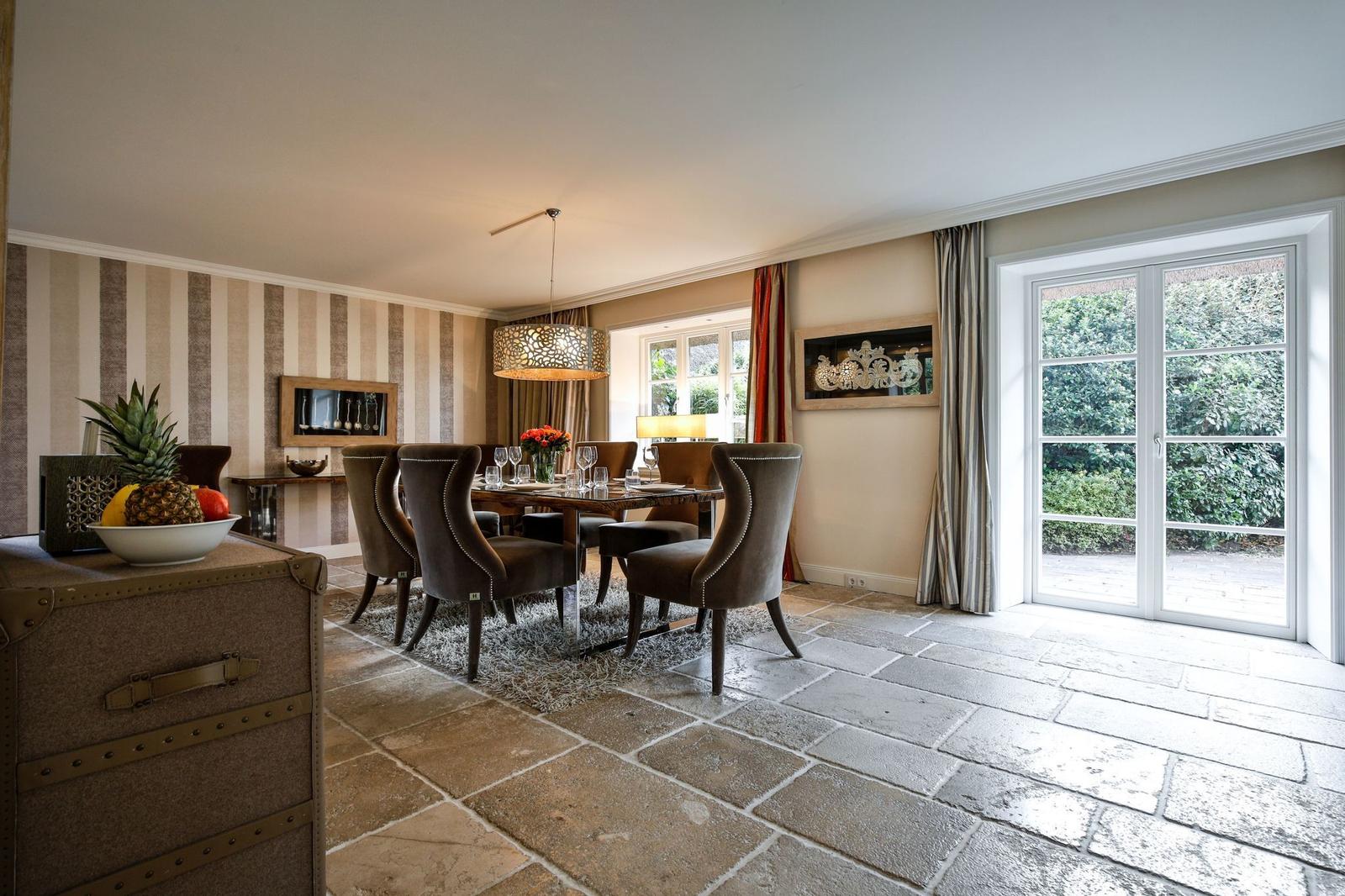 Esszimmer mit Tisch, Stühlen und Steinboden. Fenster und Glastür zu Garten.