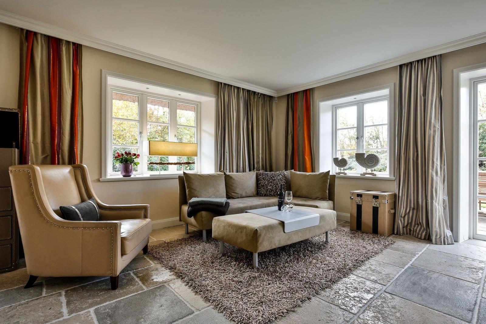 Wohnzimmer mit Sofa, Sessel, Teppich und Fenstern mit Vorhängen.