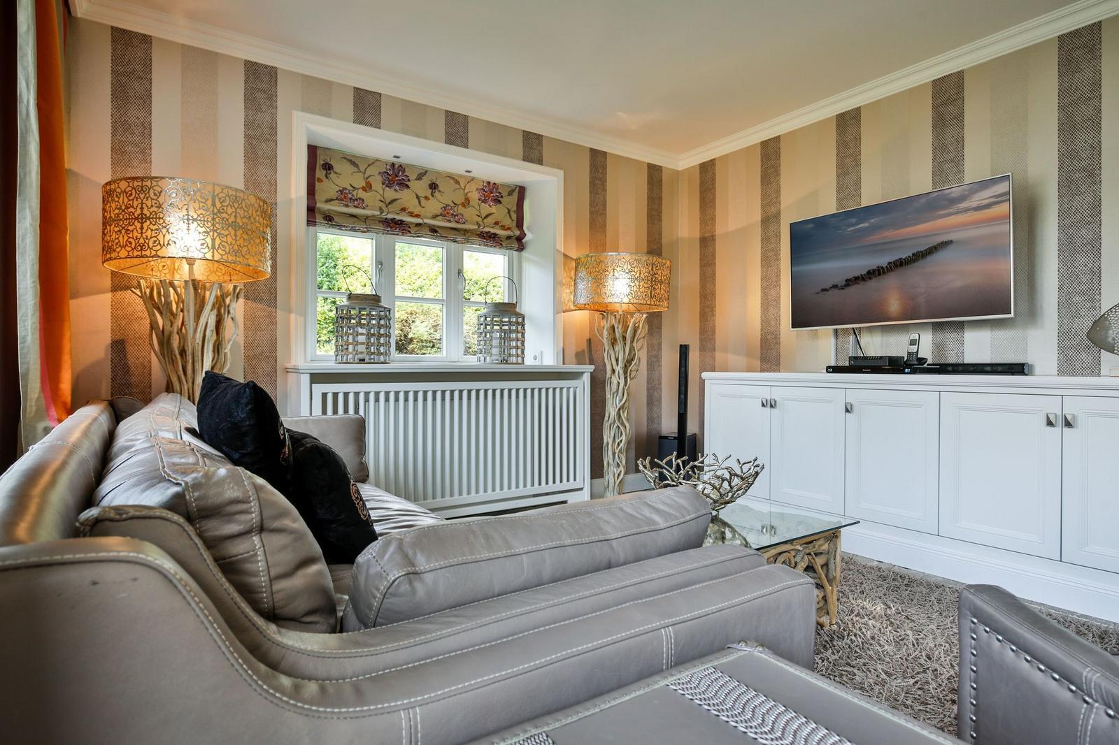 Ein Wohnzimmer mit grauem Sofa, TV und gestreifter Wandtapete.