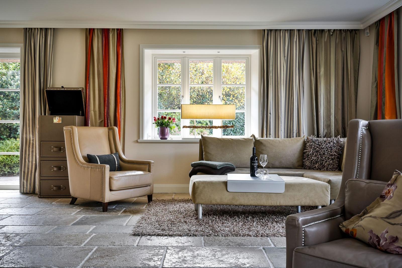 Wohnzimmer mit Ledersofa, Sessel und Fenster mit Blick auf Garten