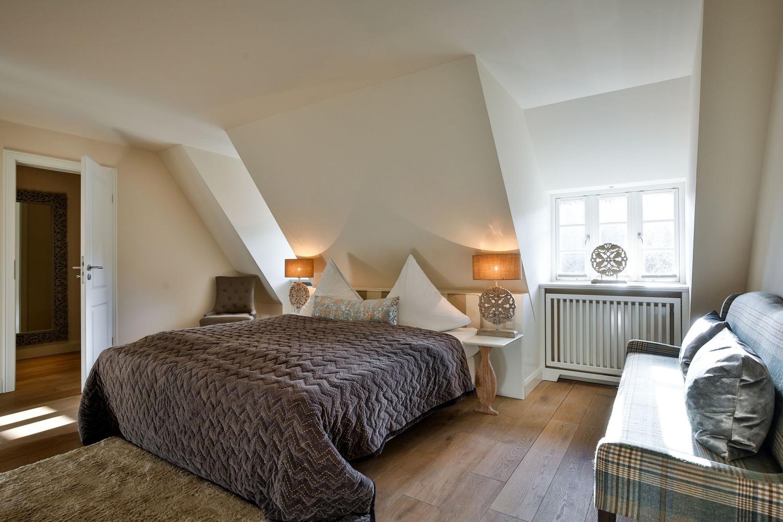 Schlafzimmer mit Dachschrägen, Bett, Sofa und Fenster.