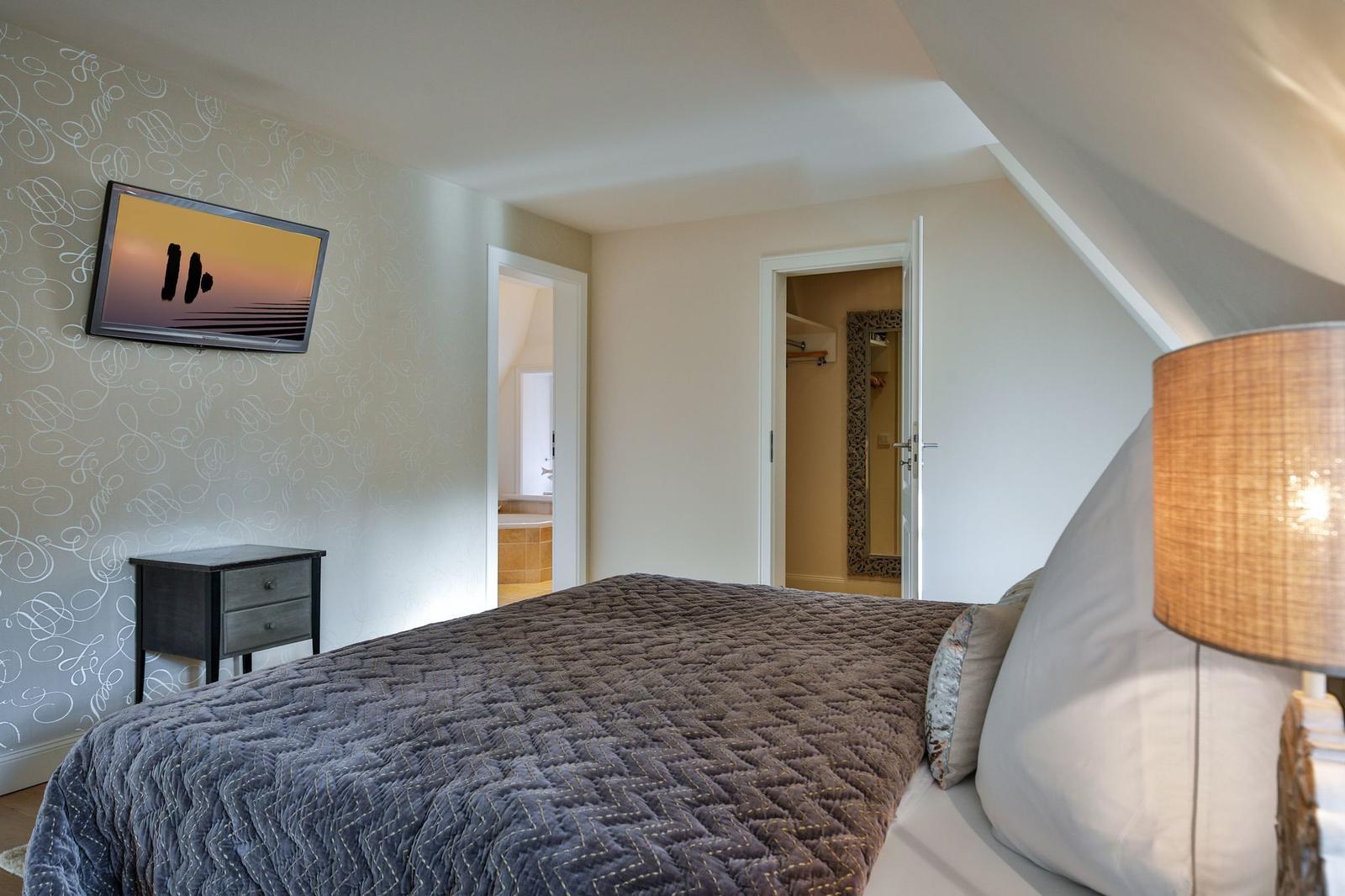 Schlafzimmer mit Bett, Nachttisch und Wand-TV. Blick in Badezimmer und Kleiderschrank.