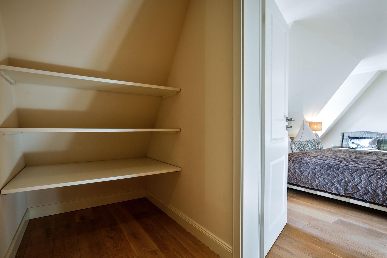 Schlafzimmer mit Dachschräge und Kleiderschrank mit drei Regalen.