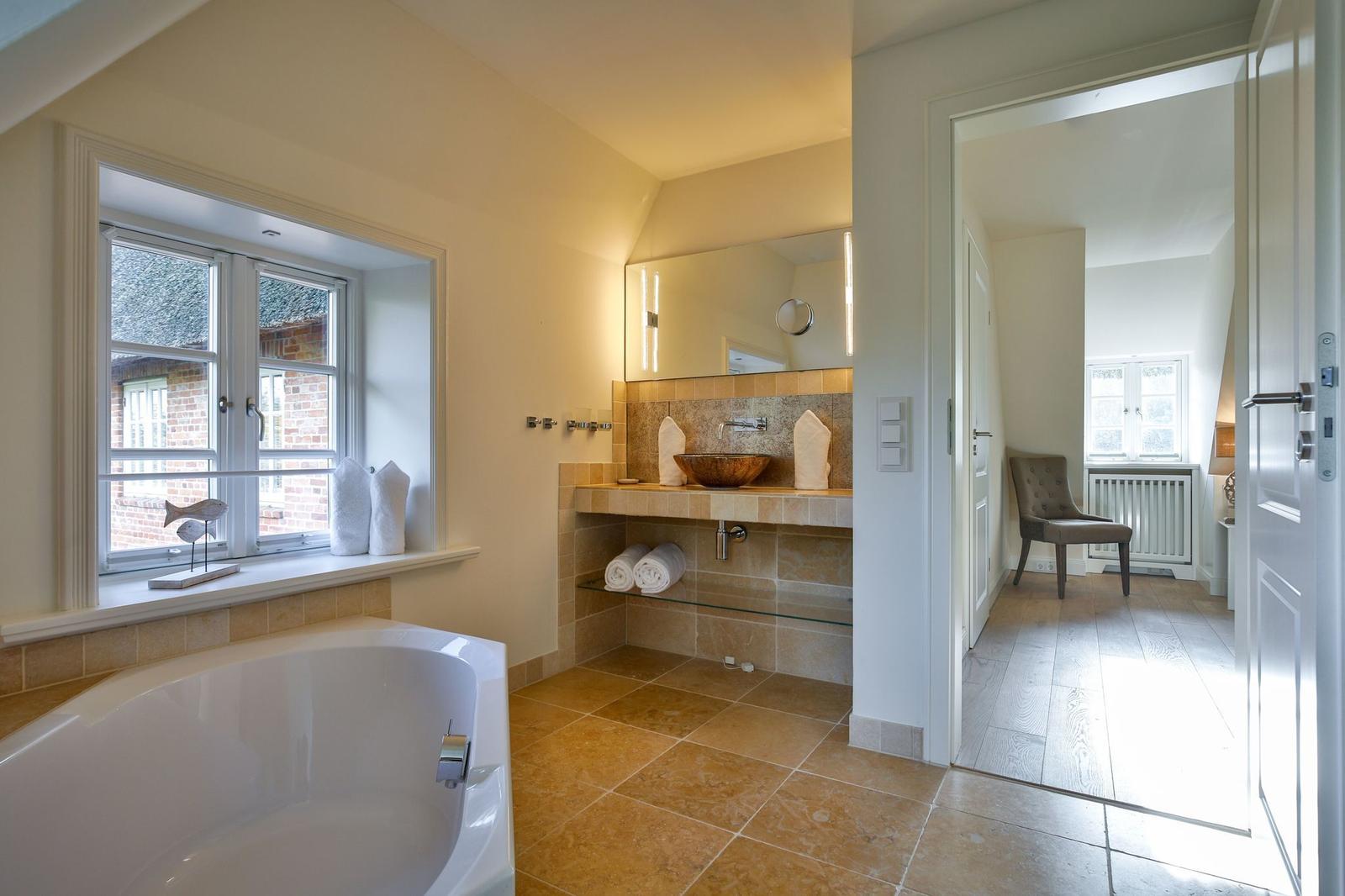 Badezimmer mit Badewanne, Waschtisch und Blick in Schlafzimmer.
