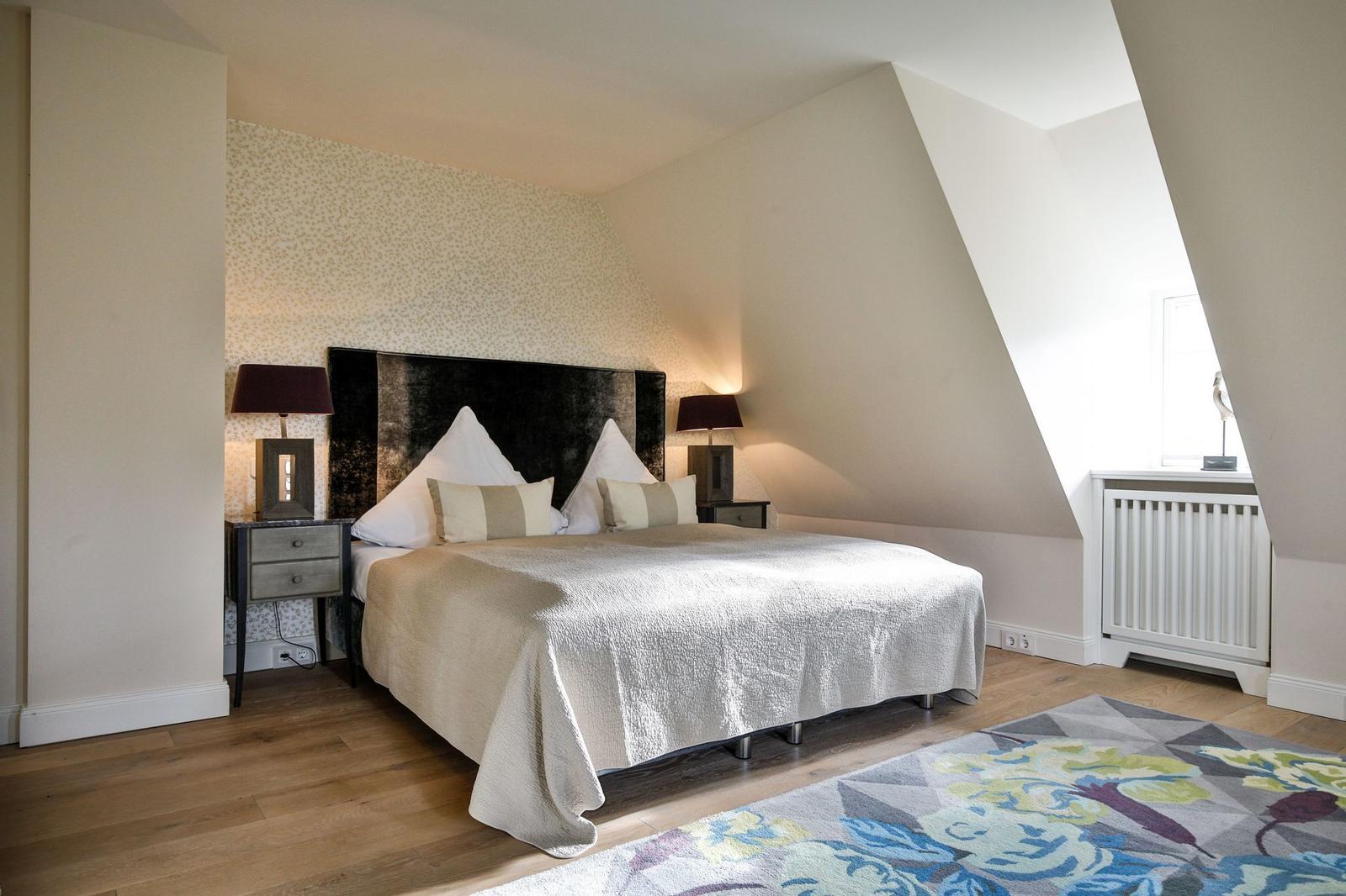 Schlafzimmer mit Dachschrägen, Bett, zwei Nachttische und Teppich.