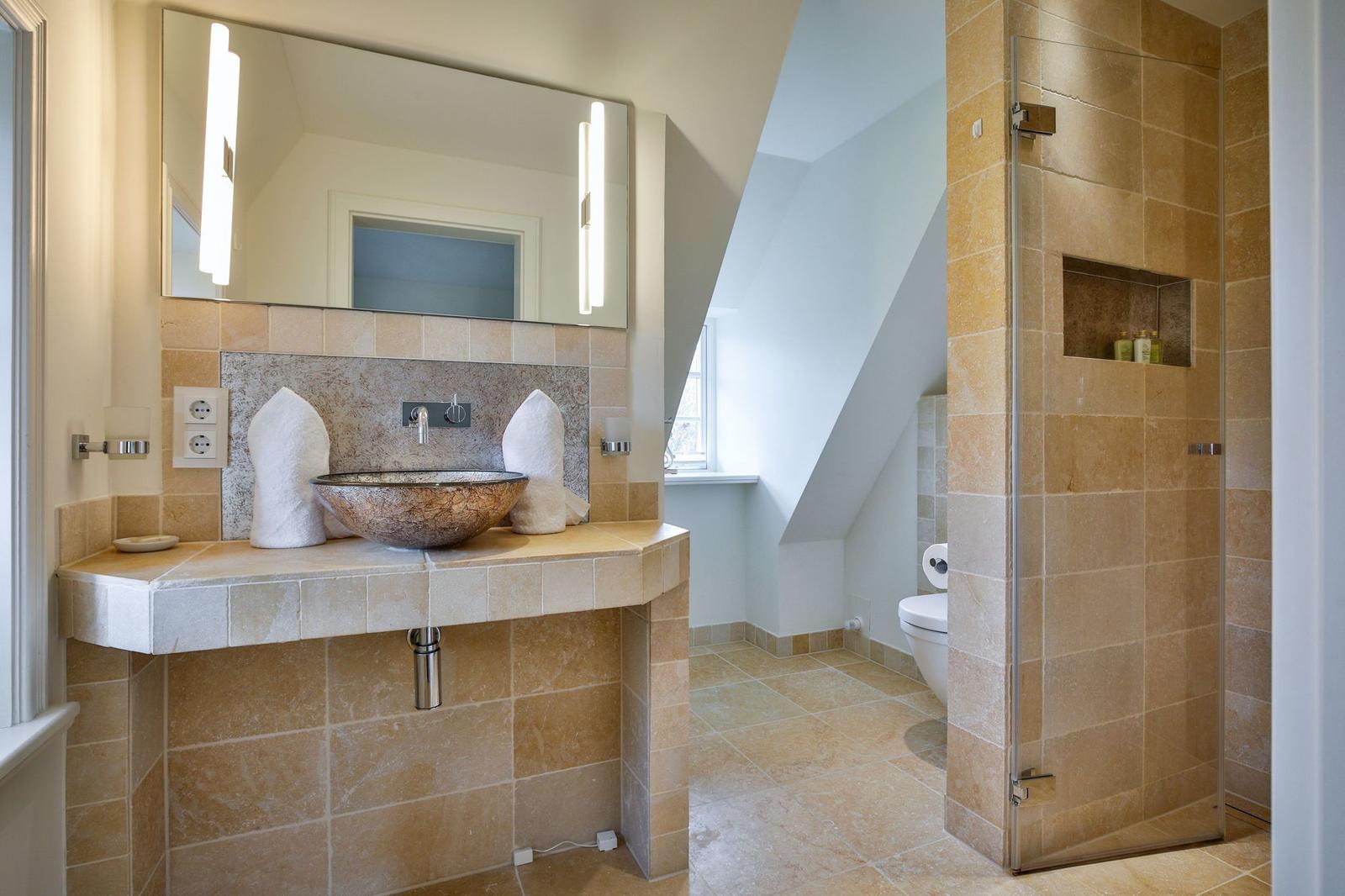 Bad mit Dusche, Waschtisch und Toilette. Fliesen und Spiegel sichtbar.