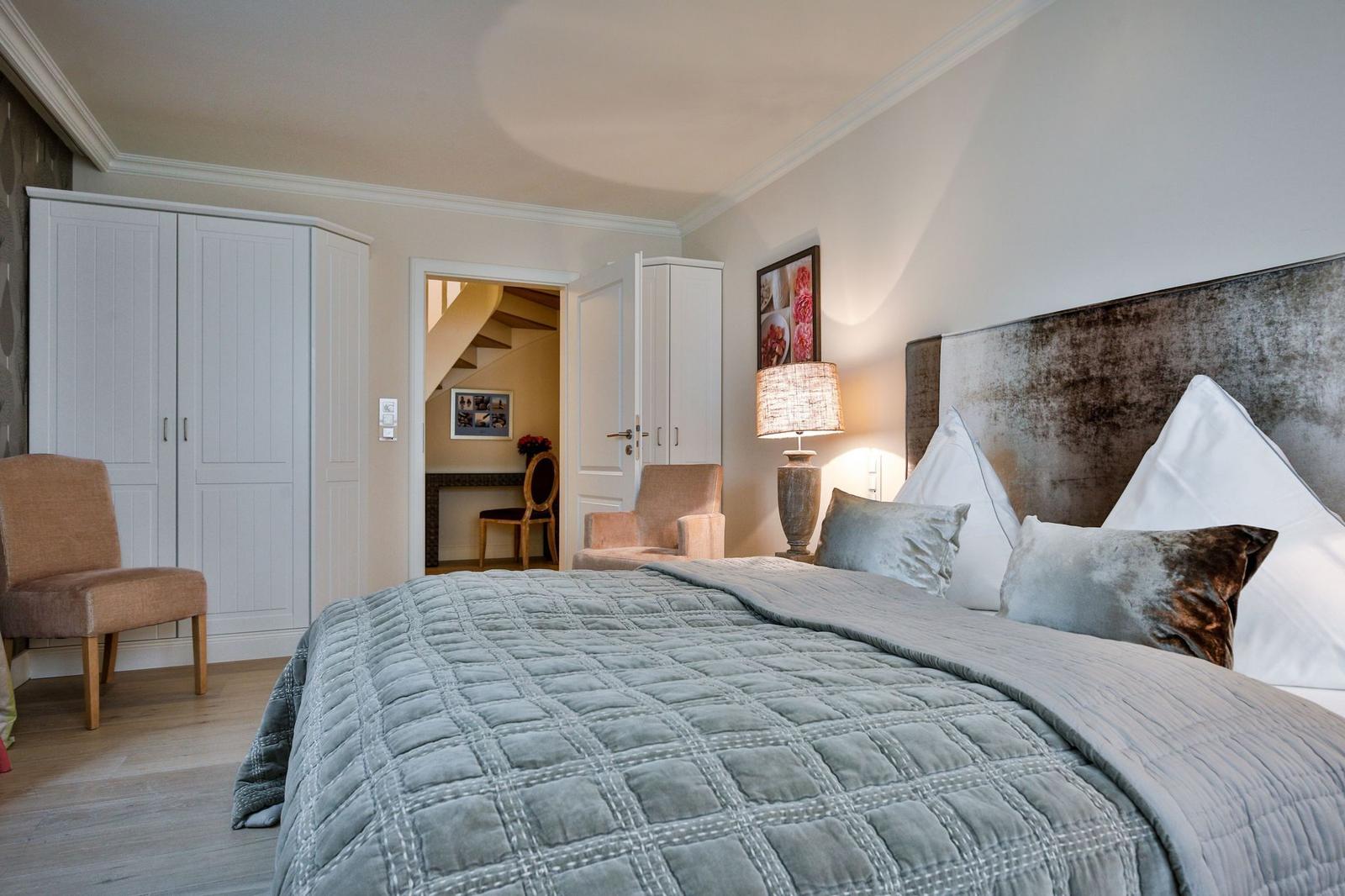 Schlafzimmer mit Bett, Kleiderschrank und Sessel. Durchgang zu einer Treppe.
