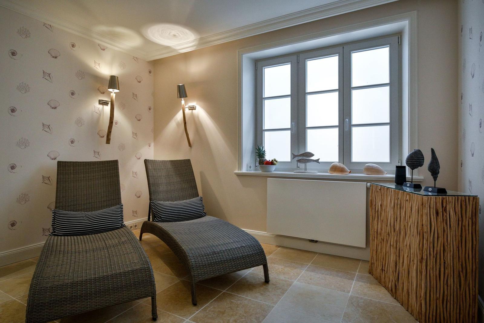 Zwei Liegestühle mit Kissen stehen vor einem Fenster. Wand mit Muster und Holzkonsole.