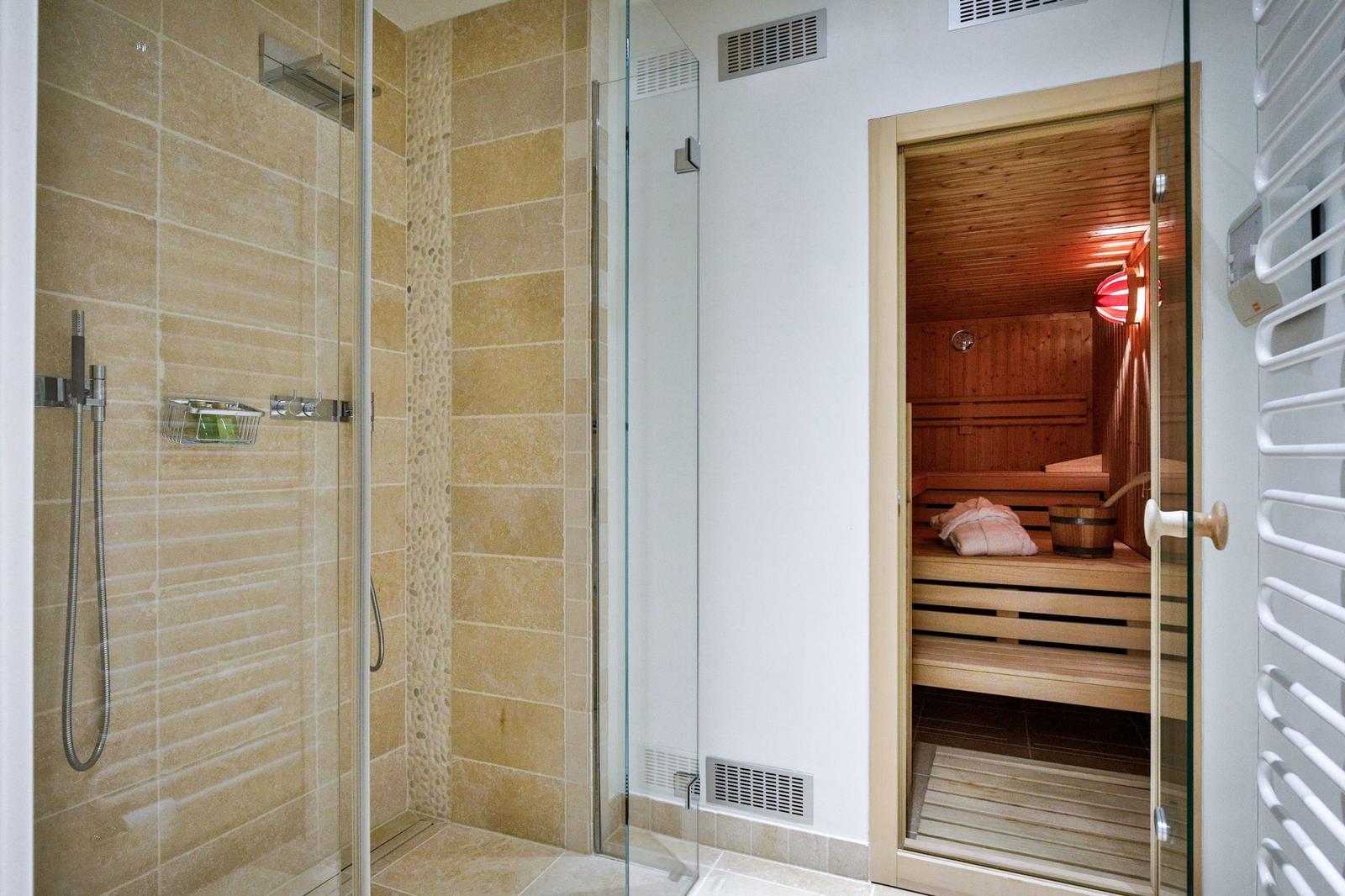 Dusche mit Glaswand und Sauna mit Holzbank und Heizung