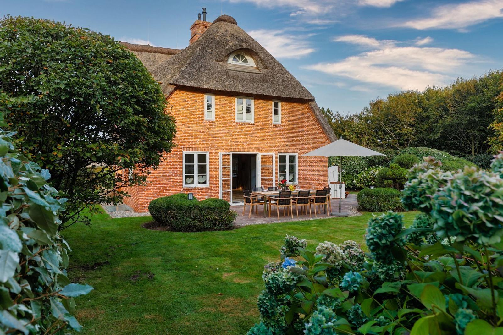 Haus mit Strohdach und Garten mit Terrasse und Tisch.