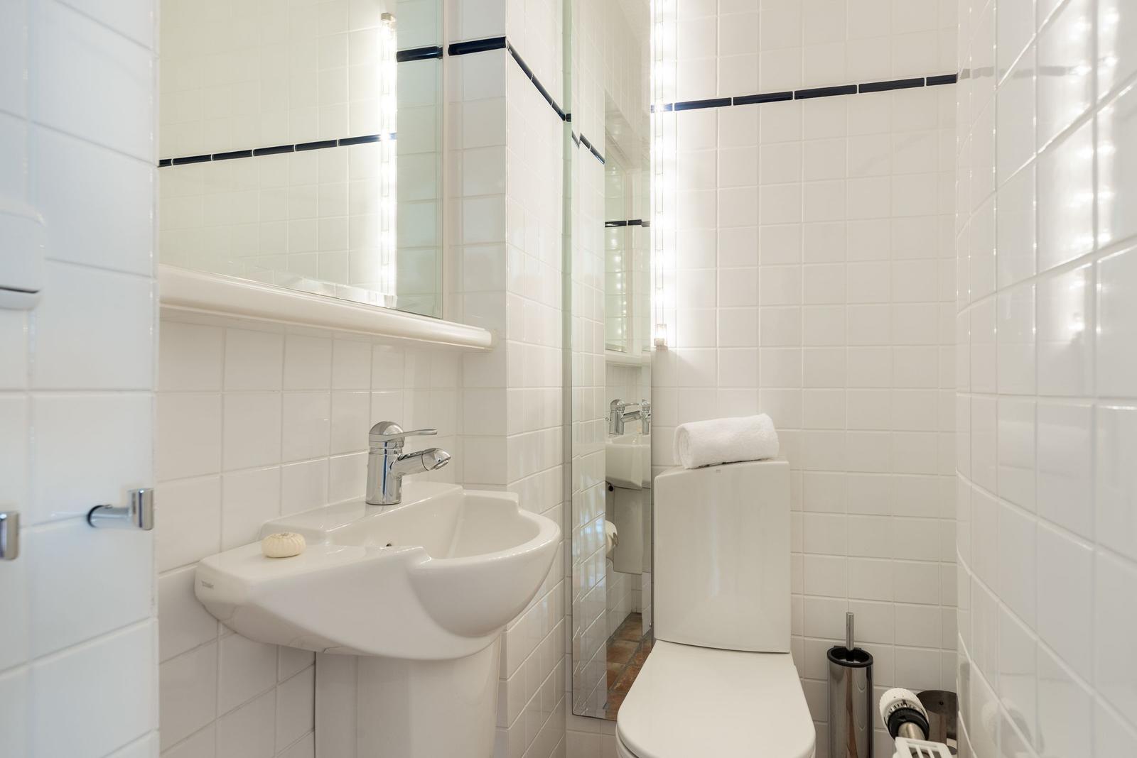 Badezimmer mit Toilette, Waschbecken und Spiegel mit Beleuchtung.