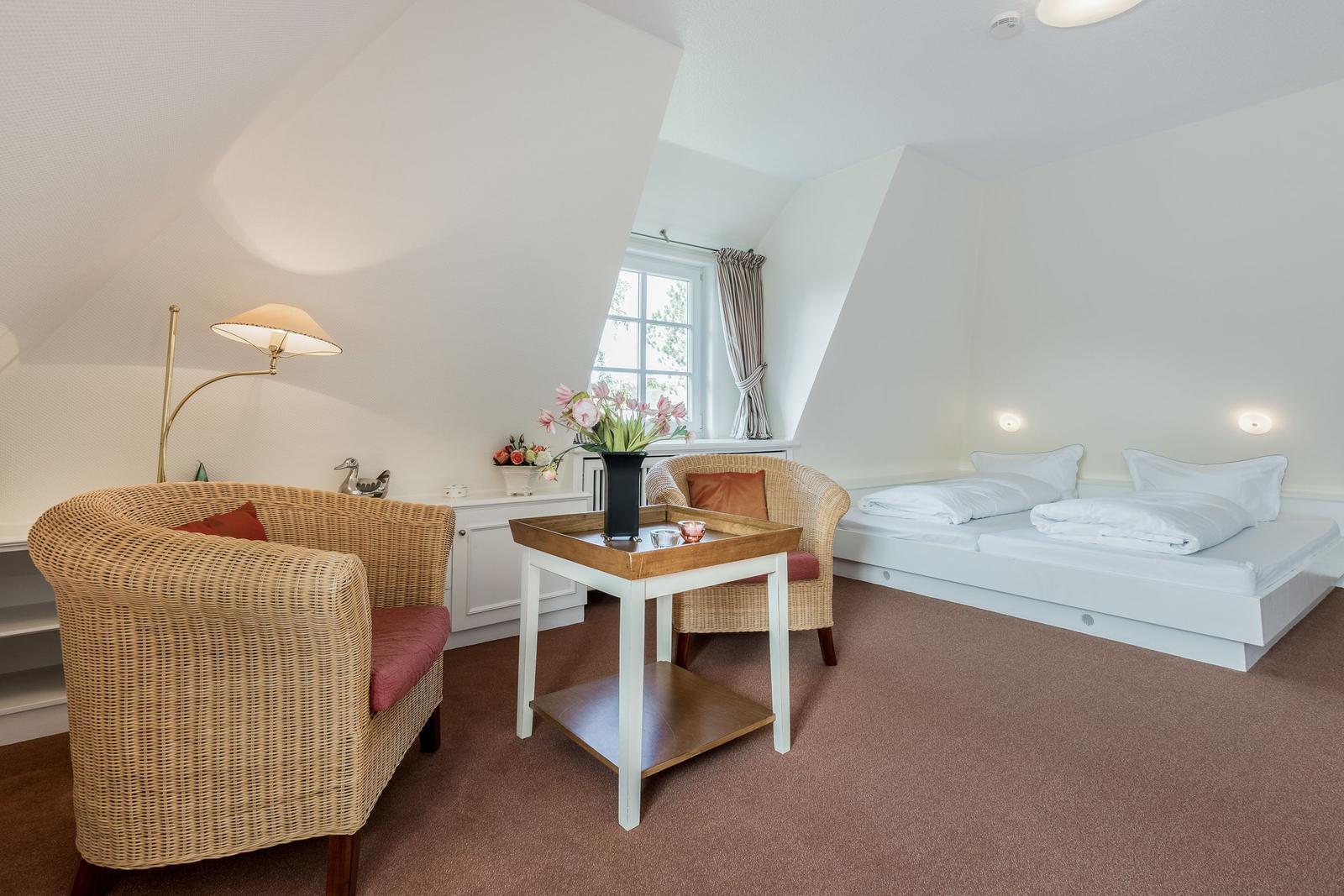 Zimmer mit Doppelbett, zwei Stühlen und Tisch unter Dachschrägen.