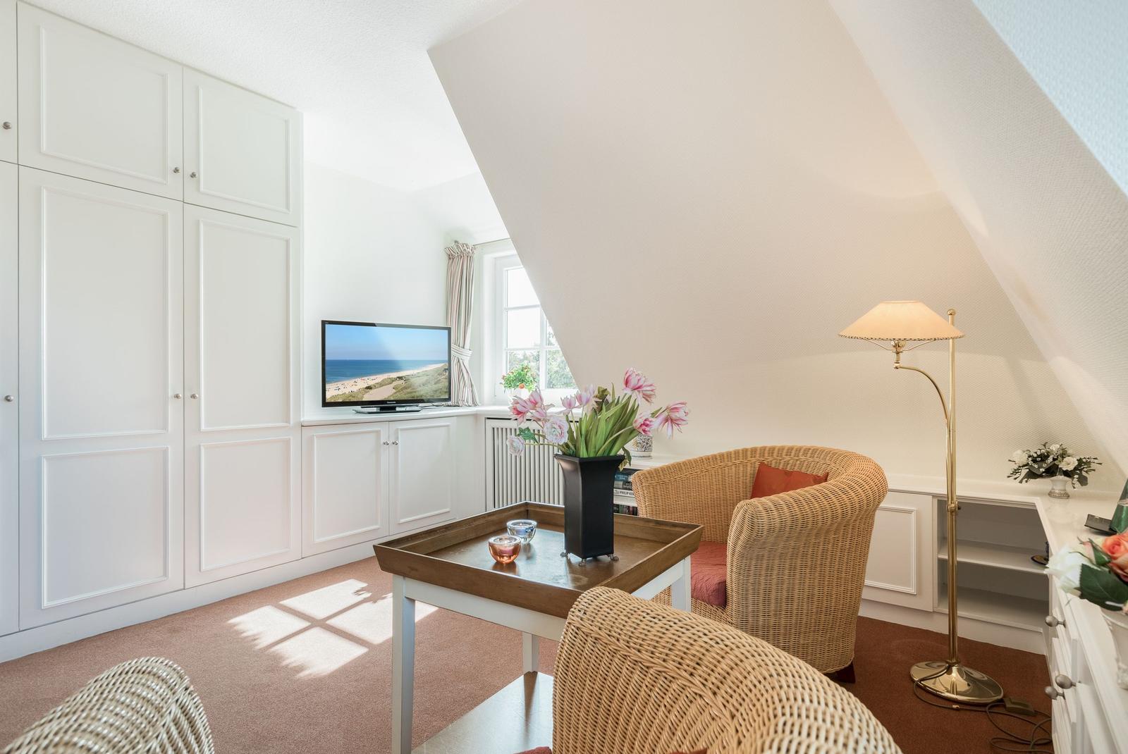 Wohnraum mit Schrank, Fernseher, Sessel und Tisch unter Dachschräge.