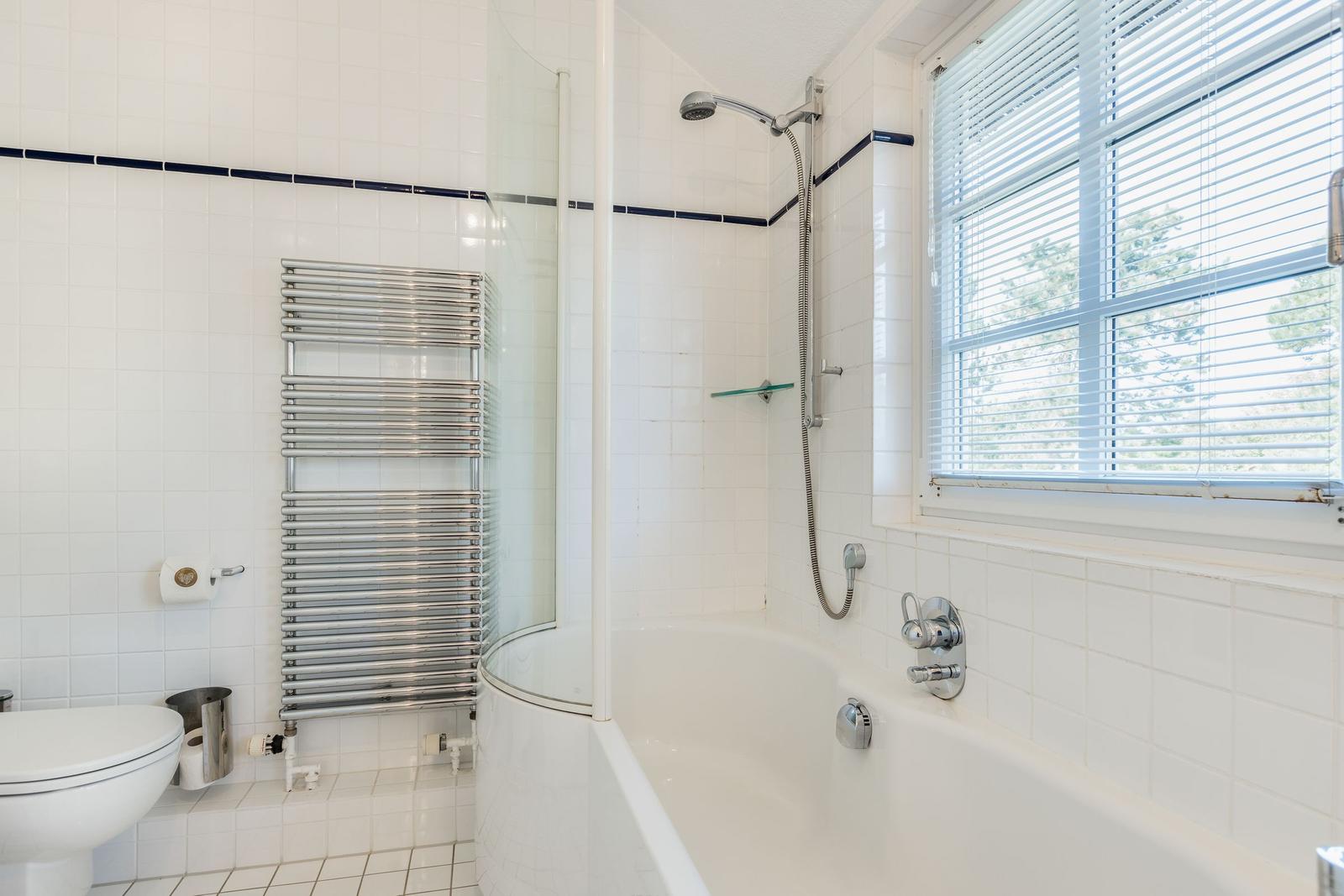 Badezimmer mit Badewanne, Dusche, Toilette und Heizkörper.