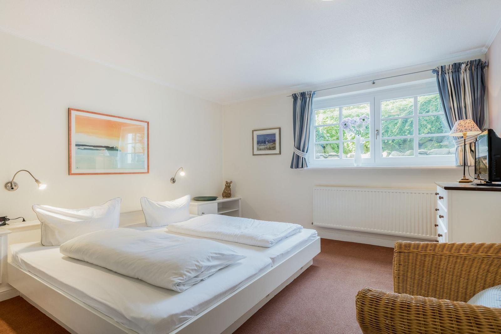 Schlafzimmer mit Bett, Fenster und Wickerstuhl.