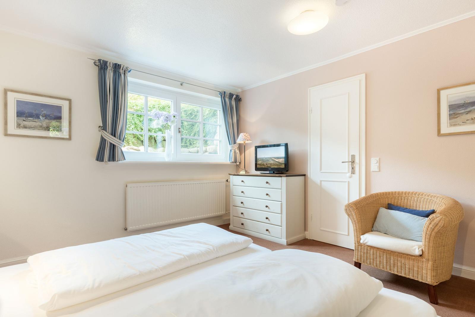 Schlafzimmer mit Bett, Schrank, Fernseher und Sessel. Fenster mit Blick auf Grün.