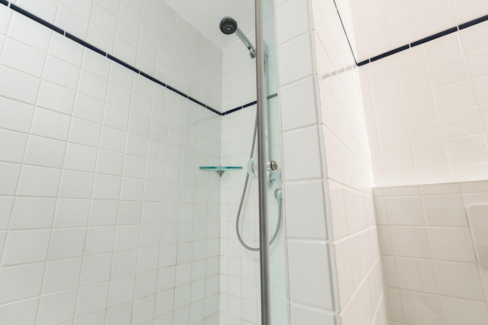 Dusche mit Glaswand, weißen Fliesen und dunkler Zierleiste