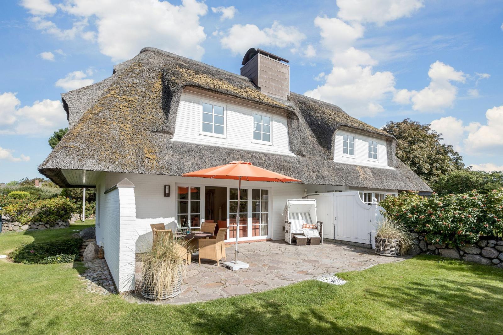 Haus mit Strohdach, Terrasse mit Sonnenschirm und Garten.
