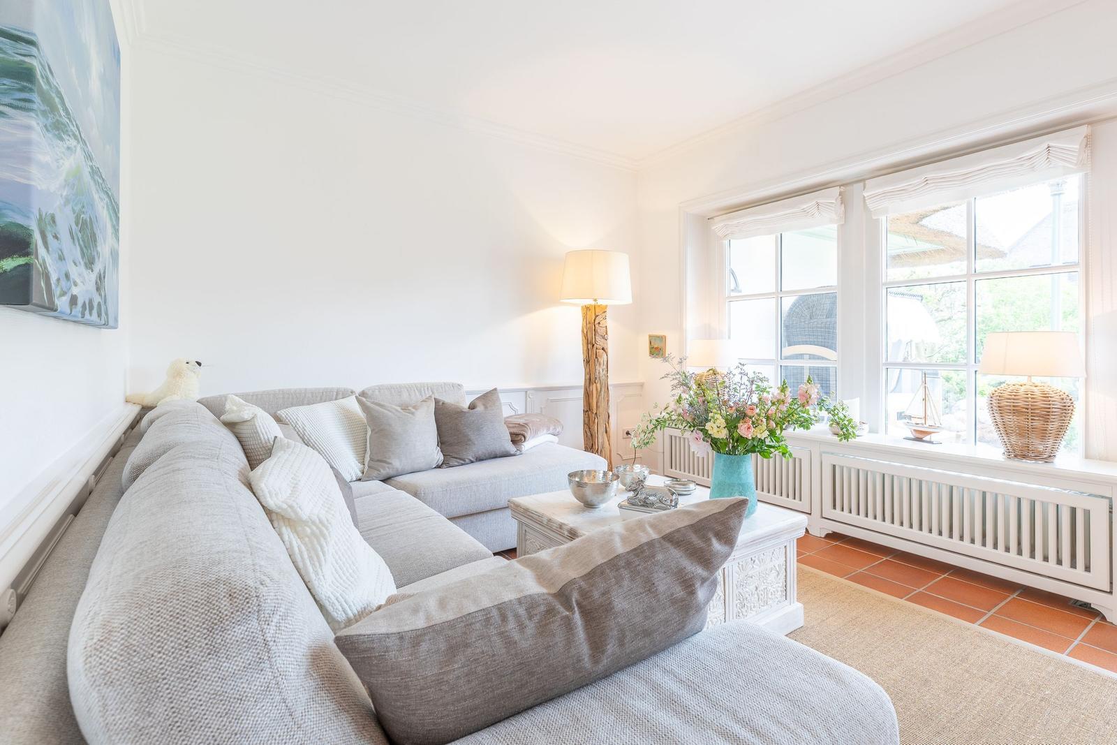 A living room with a gray sofa, a table, and windows with a view outside.