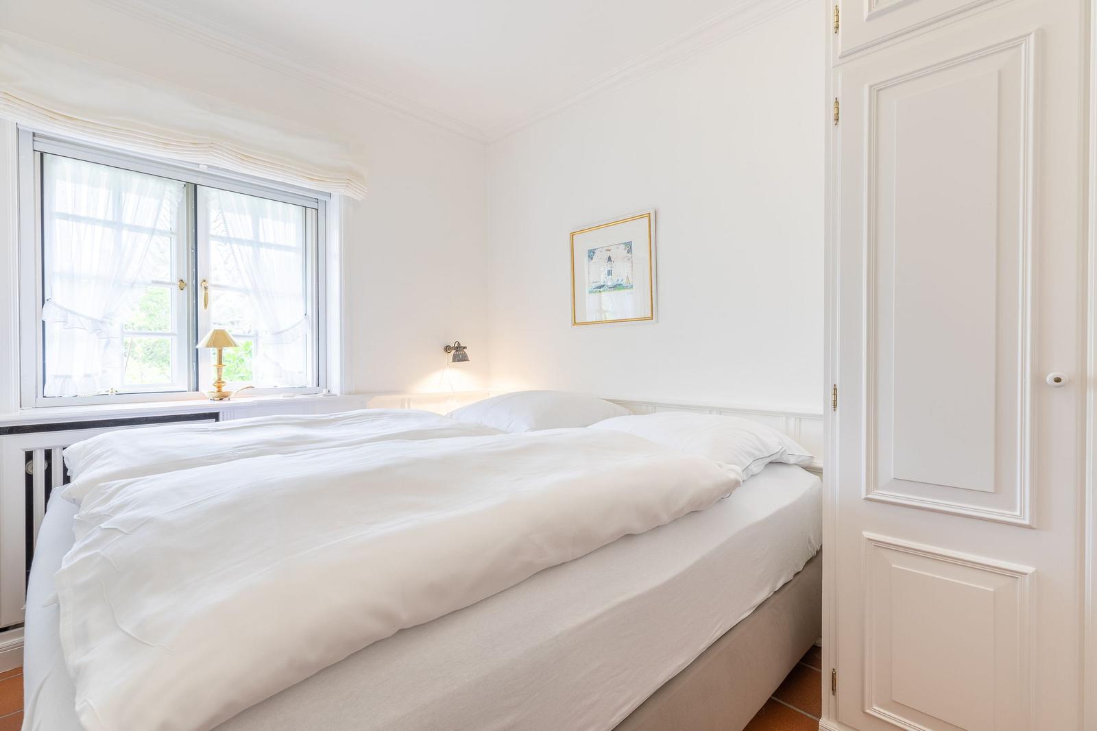 A bedroom with a white bed, window, and door.