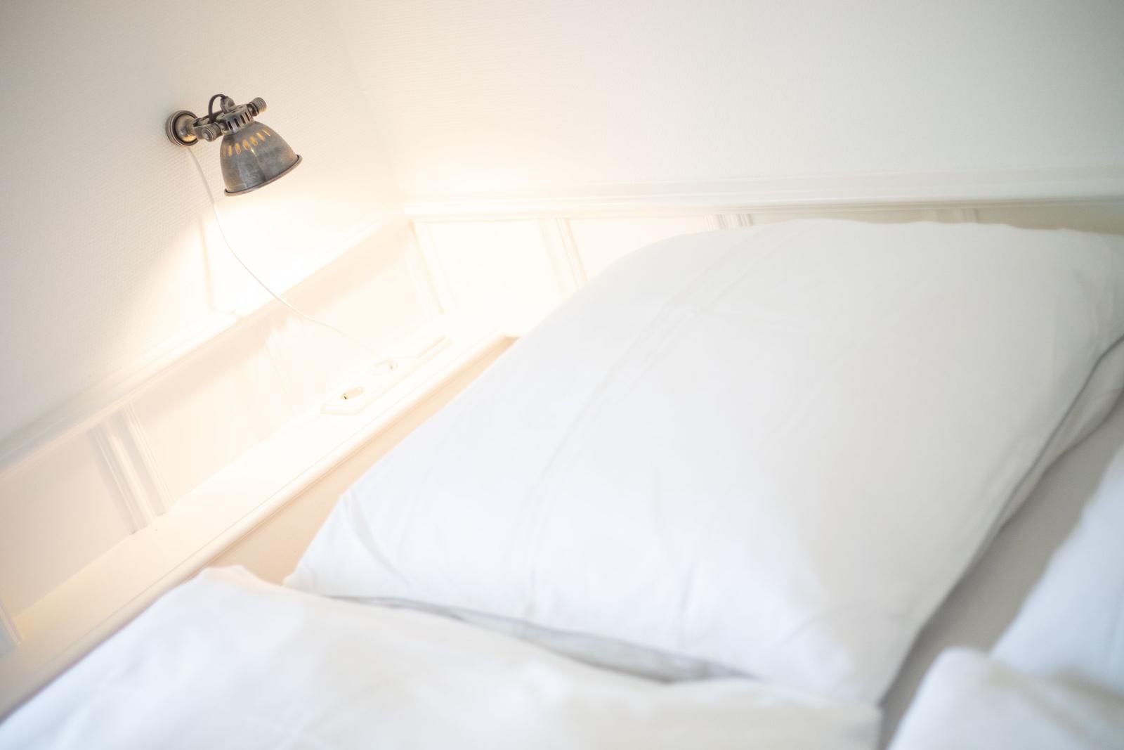 Headboard with white bedding and wall lamp.