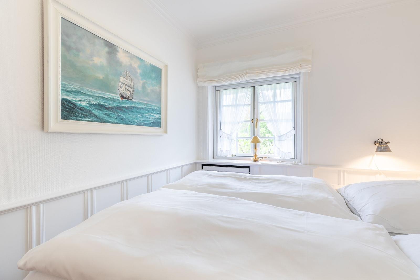 Bedroom with white bed, window, and wall painting of a sailboat.