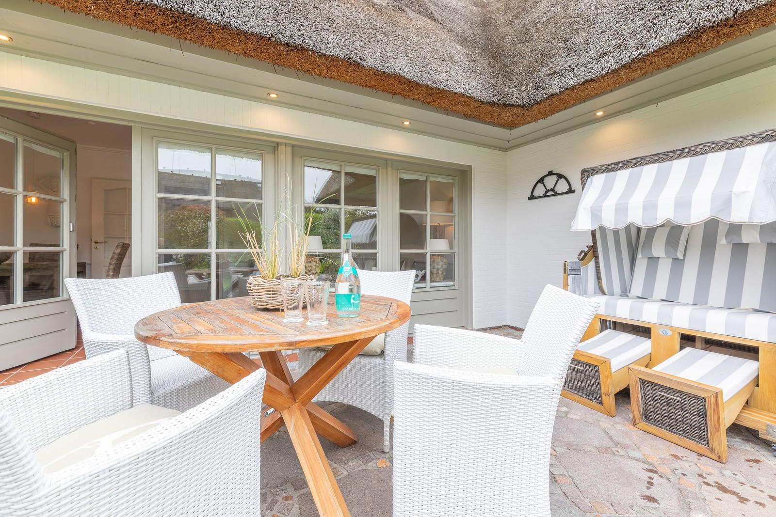 Terrace with table, chairs, and lounge under thatched roof.