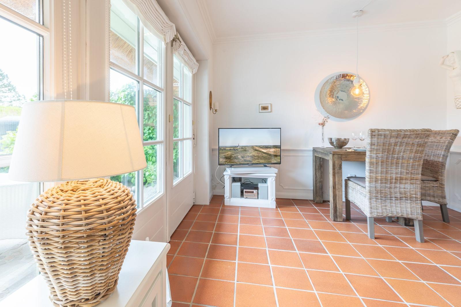 Living and dining area with terracotta floor, TV, and dining table with chairs.