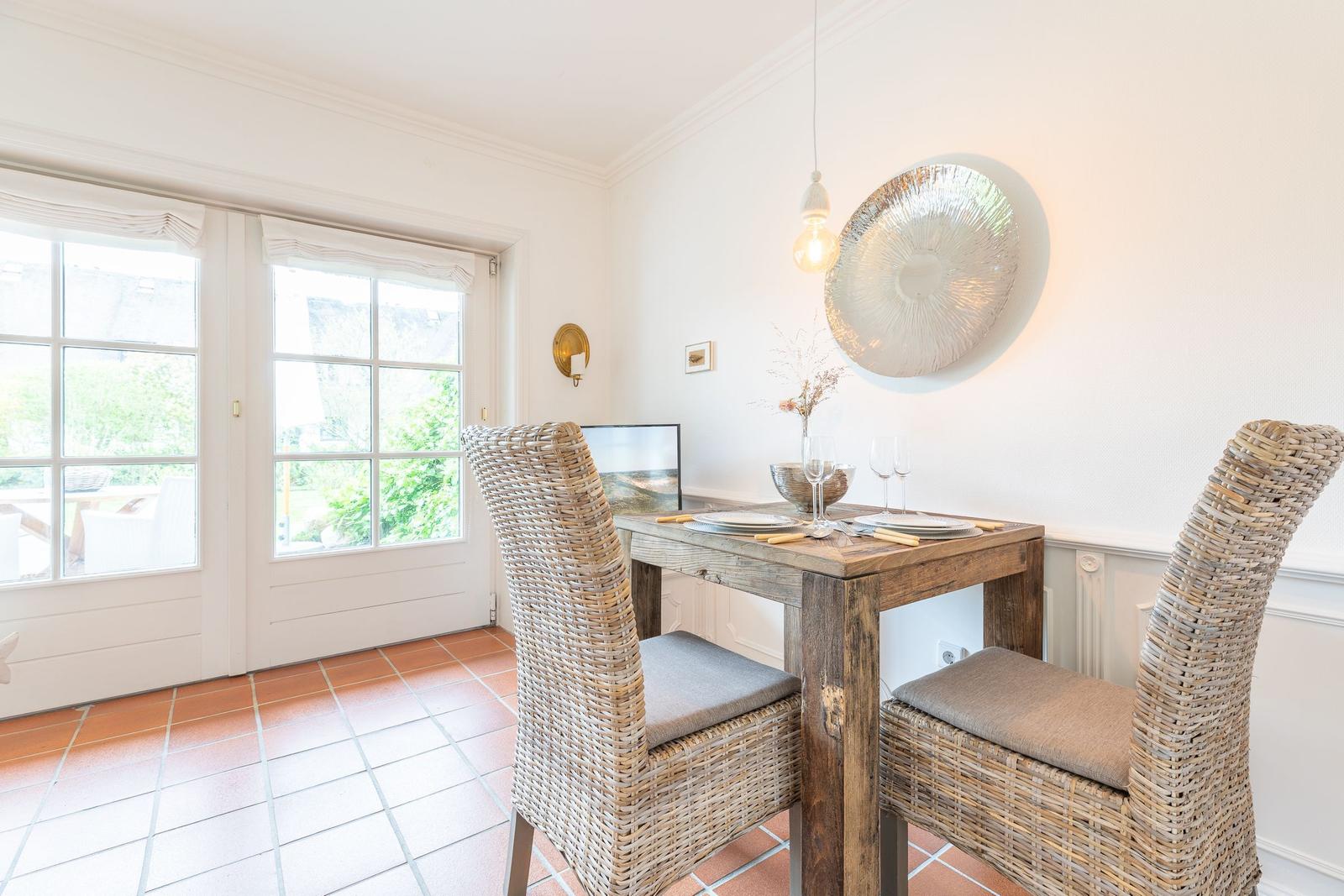 Dining room with rustic table, two wicker chairs, and view to the garden.