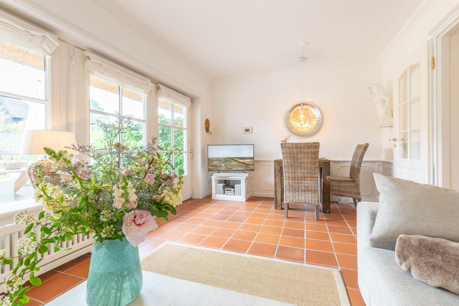 Living and dining area with terracotta floor, TV, dining table, and flower arrangement.