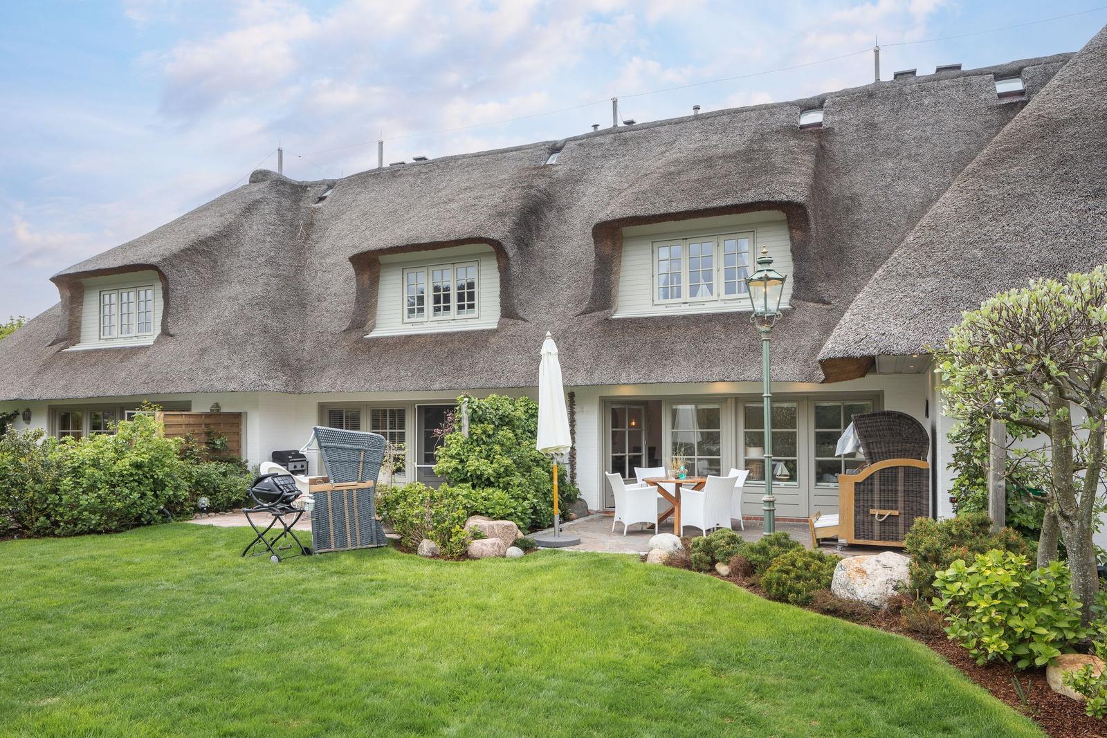 House with thatched roof, garden, and terrace with seating.