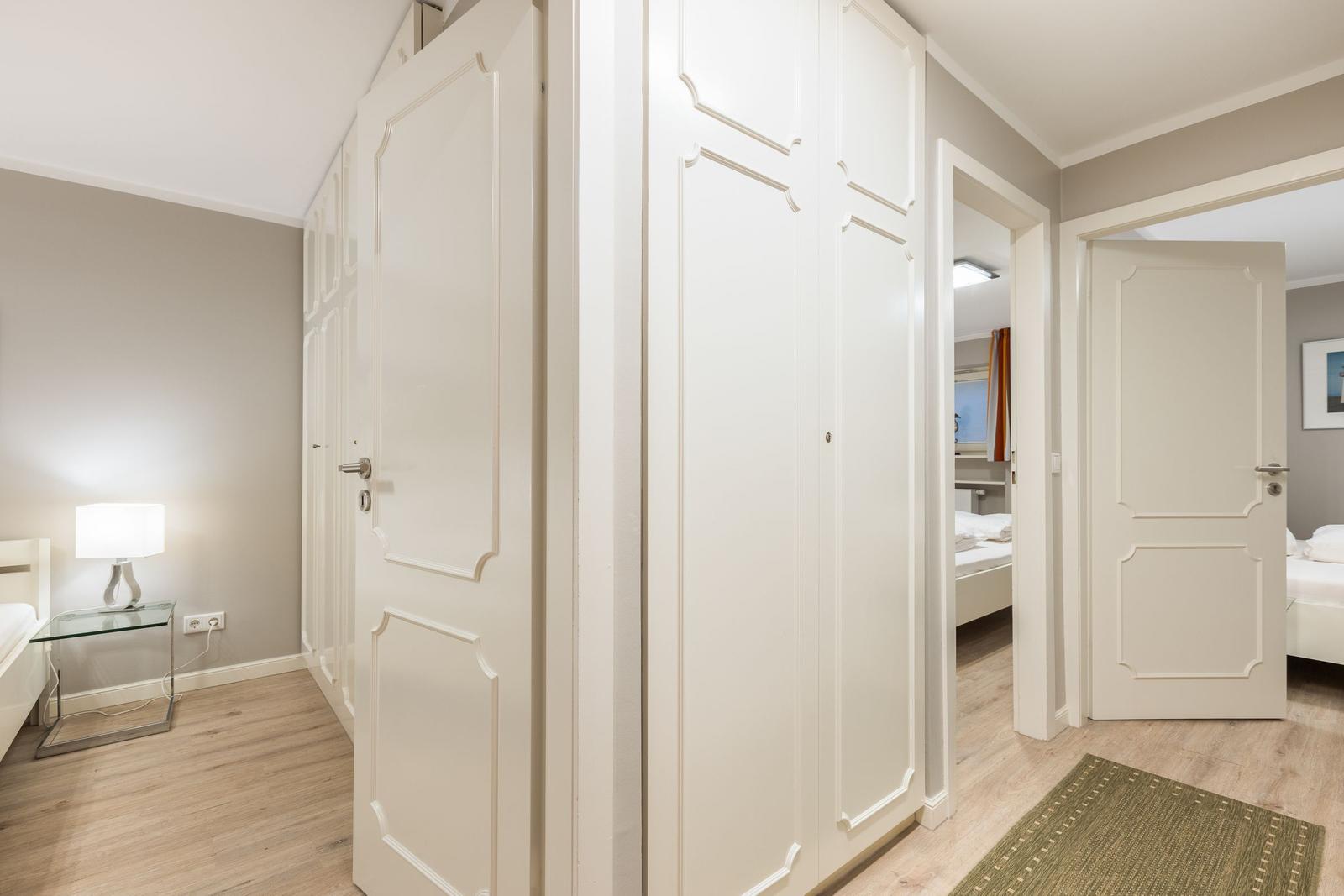 Flur mit weißen Türen und Kleiderschränken. Blick in zwei Schlafzimmer mit Betten.